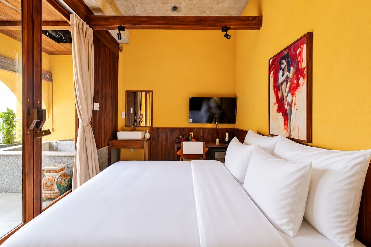 A hotel room with a large bed, a television, a bathroom with a sink, and a painting on the wall.