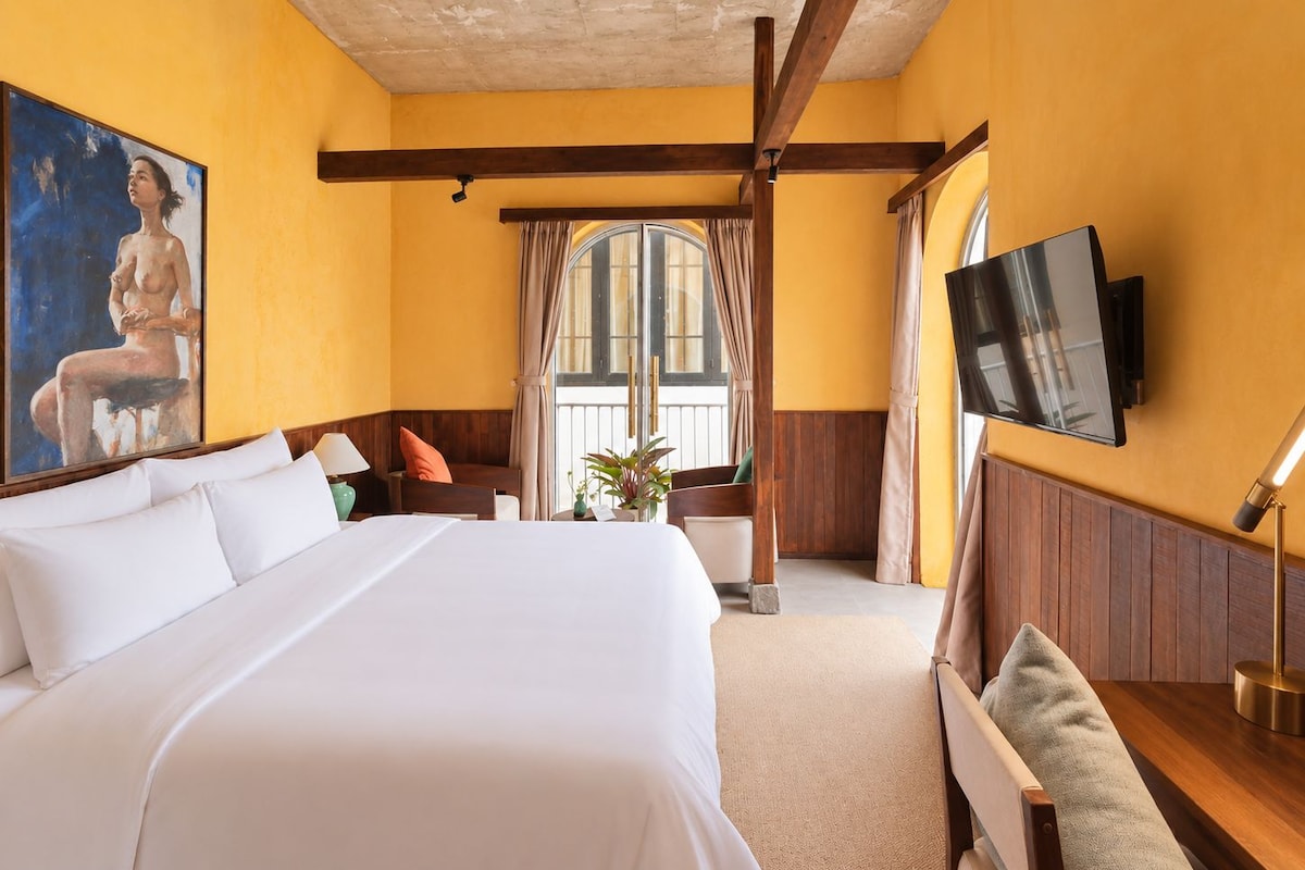 A hotel room with a large bed, a television mounted on the wall, and a window with curtains.