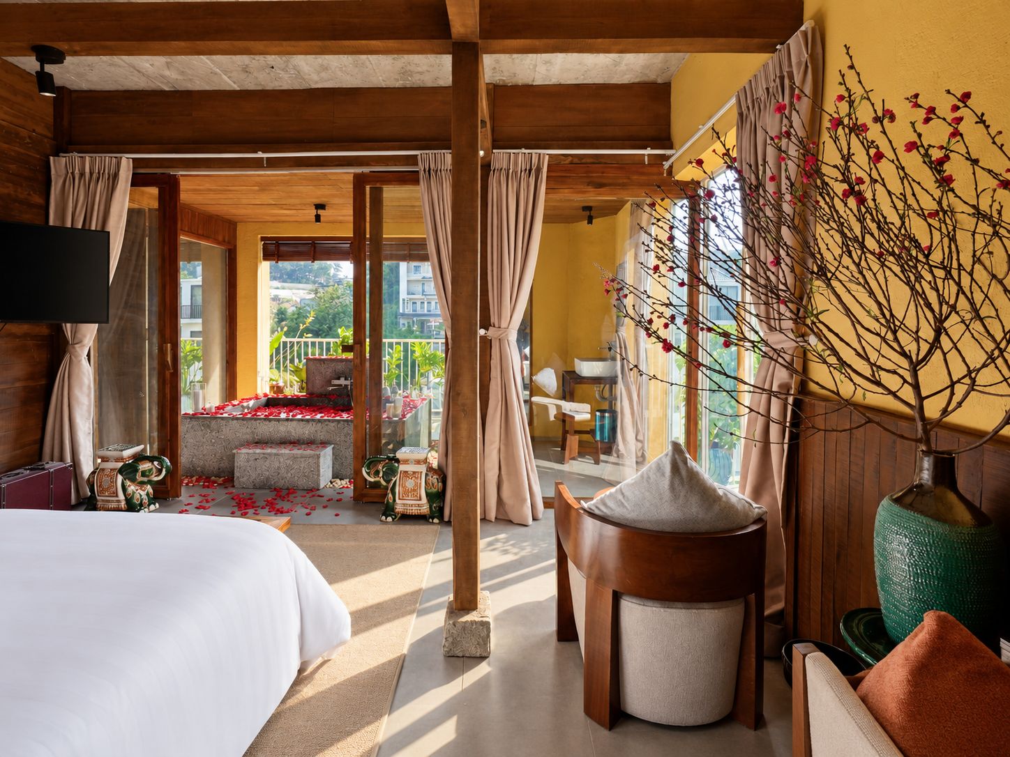 A hotel room with a bed, a small table, a chair, a sofa, a TV, and a balcony with a view of the city.