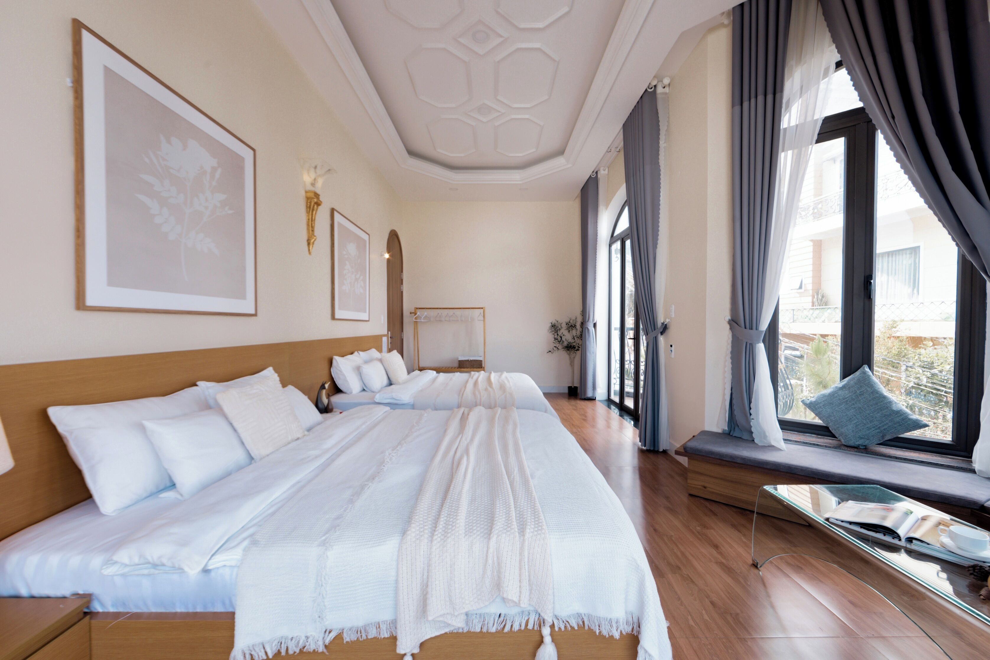 Un dormitorio espacioso con una cama grande, una mesita de noche, un rincón con ventanal y vistas, y un techo con diseño geométrico.