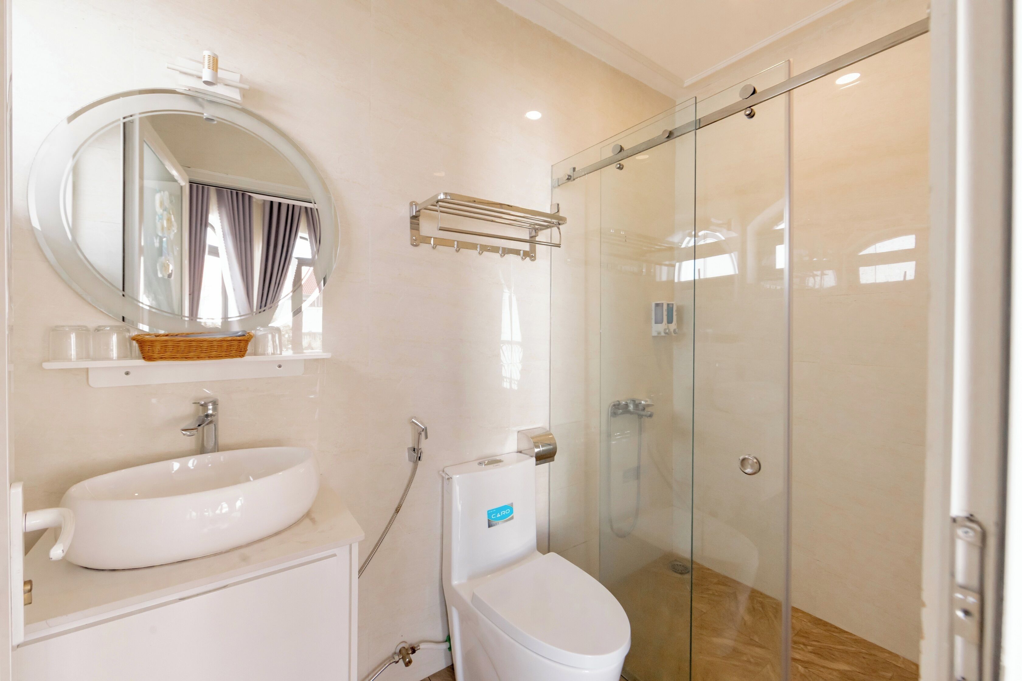 A bathroom with a round mirror, a white sink, a toilet, and a glass shower enclosure.