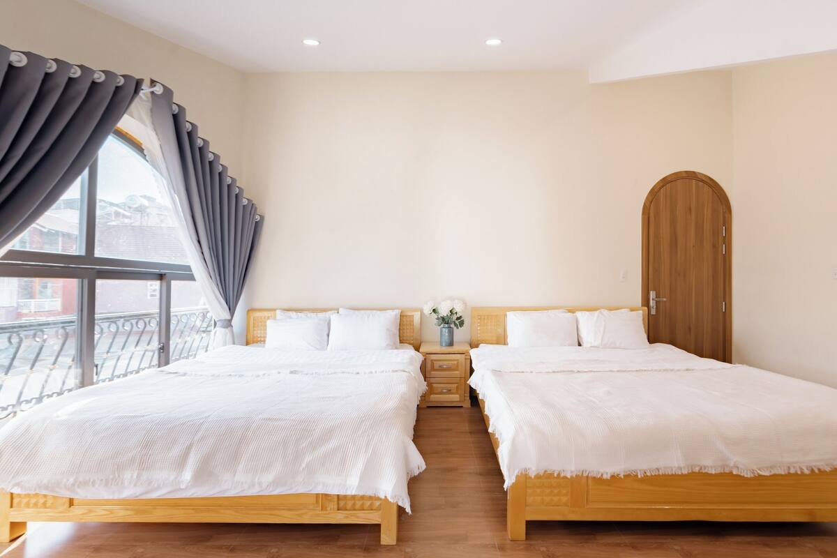 Een hotelkamer met twee bedden, een houten garderobe, een nachtkastje met een vaas, en een raam met gordijnen.