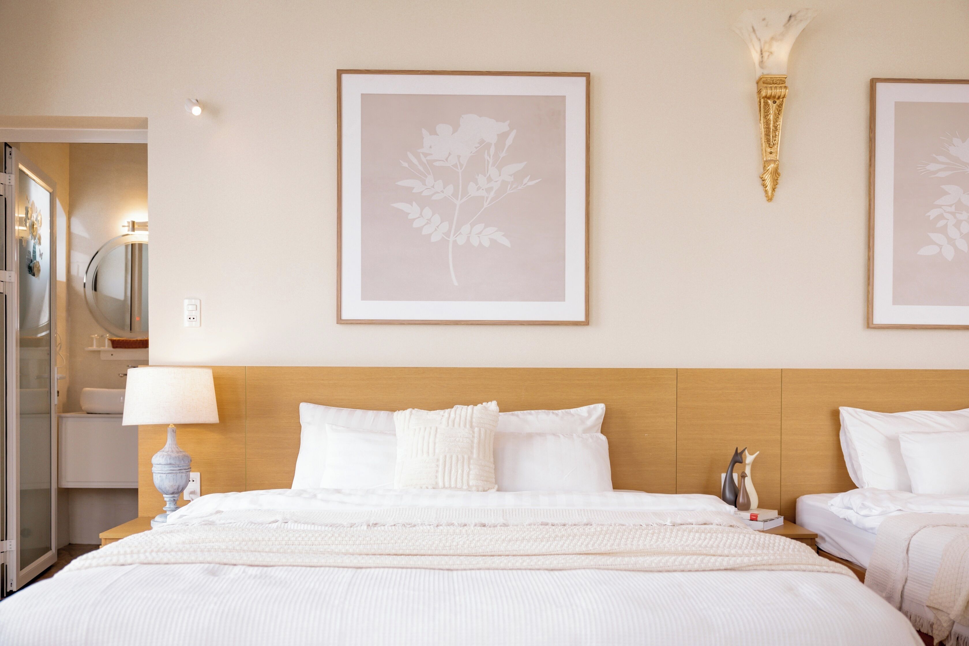 Une chambre d’hôtel avec un grand lit, une table de chevet avec une lampe et deux œuvres d’art florales encadrées accrochées au mur.