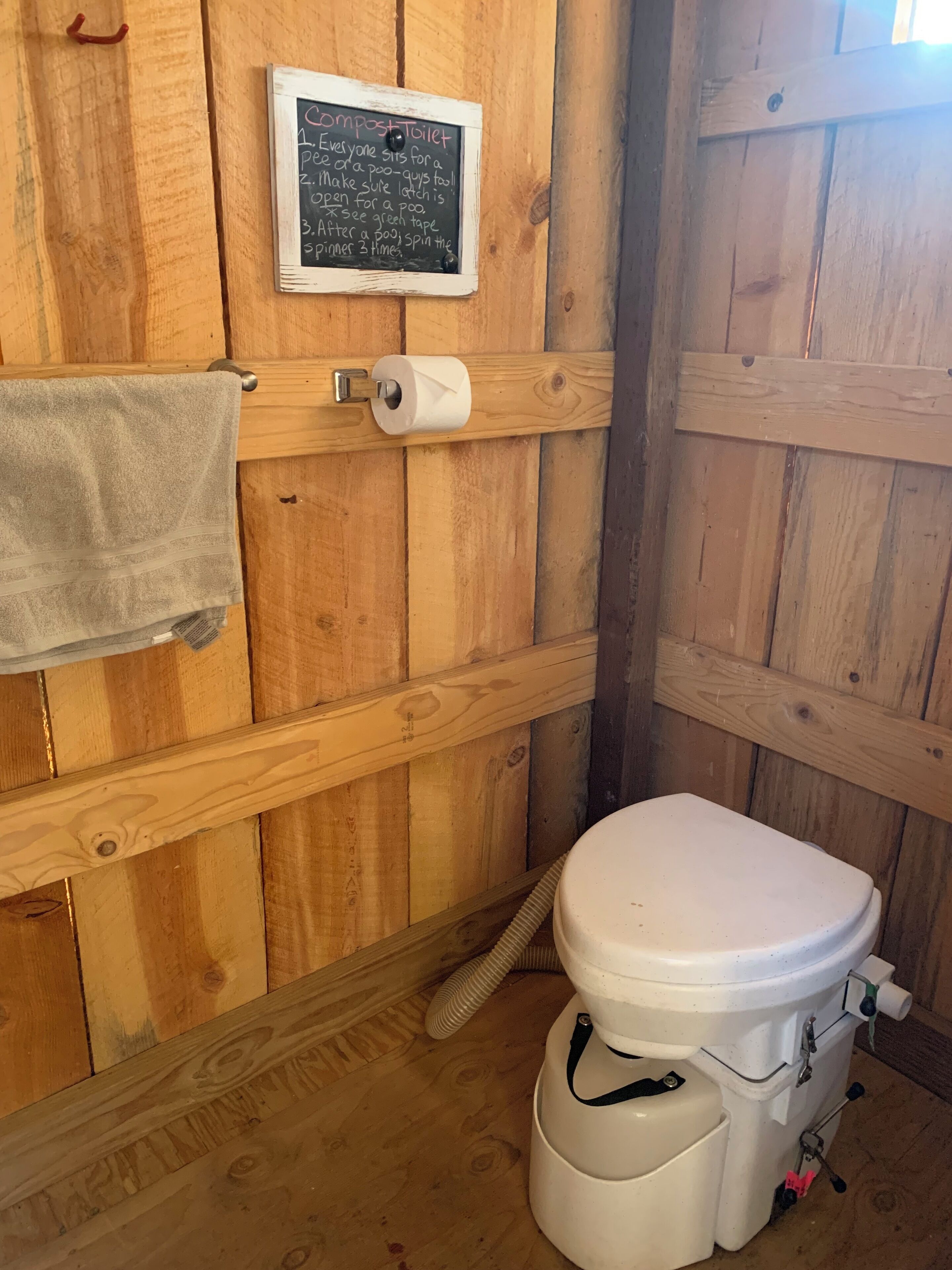 Un baño de madera con inodoro, una toalla colgada en la pared y una pizarra con indicaciones.