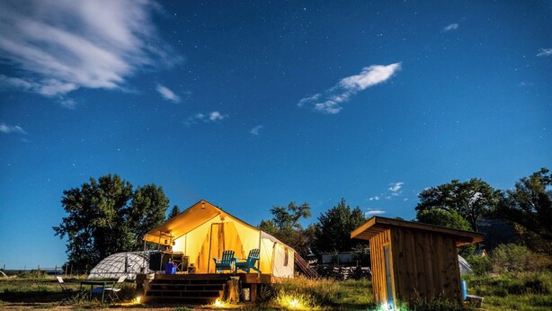 A cozy outdoor accommodation with a tented structure, a wooden cabin, and a clear night sky.