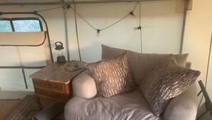 A cozy interior with a sofa, patterned pillows, a small wooden table with a lantern, and a view through a window.