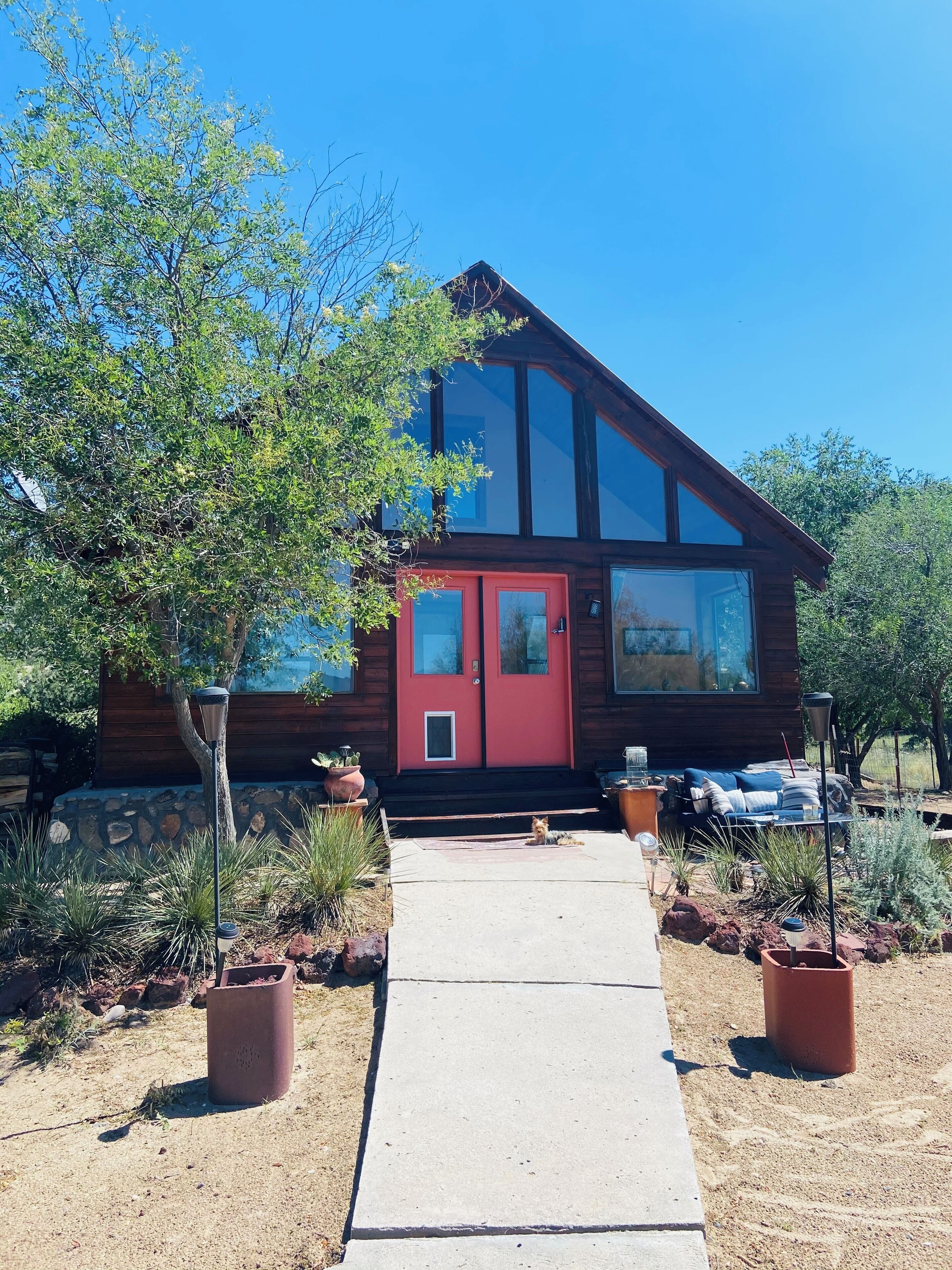 A modern house with a red door, large windows, and a stone foundation.