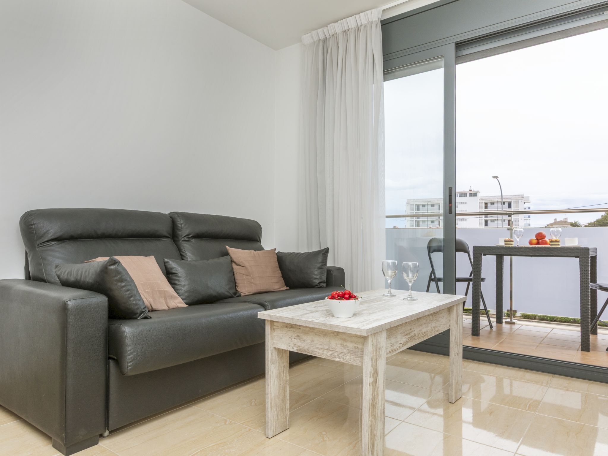 Ein modernes Wohnzimmer mit einer schwarzen Ledersofa, einem Holztisch und einem Balkon mit einem Tisch für zwei Personen.