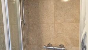Een douche met glazen wanden, een handdouche en een kraan op de muur.