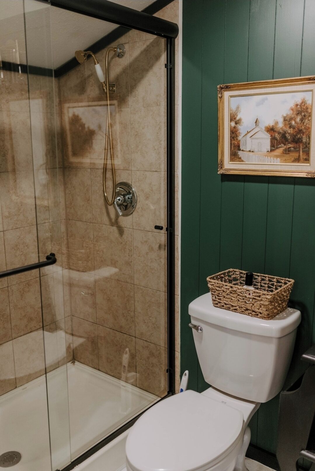 A bathroom with a glass-enclosed shower, a white toilet, and a framed painting on the wall.