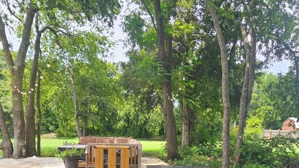 A metal swimming pool with a pump, surrounded by trees and a wooden deck with outdoor furniture.