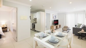 A modern living room with a dining area, a kitchen, and a TV displaying Netflix. - Smart Suites Self Check-in Apartments - 18 Darnley (Rocklea)