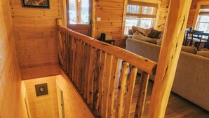 A wooden cabin interior with a staircase leading to a lofted bedroom, a living area with a sofa and a dining table.