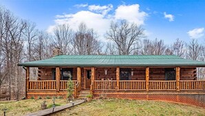 A log cabin with a green roof, wooden porch, and a fenced yard.