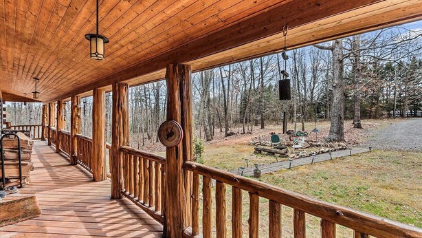 A covered wooden deck with a railing, a clock, and a view of the surrounding forest.