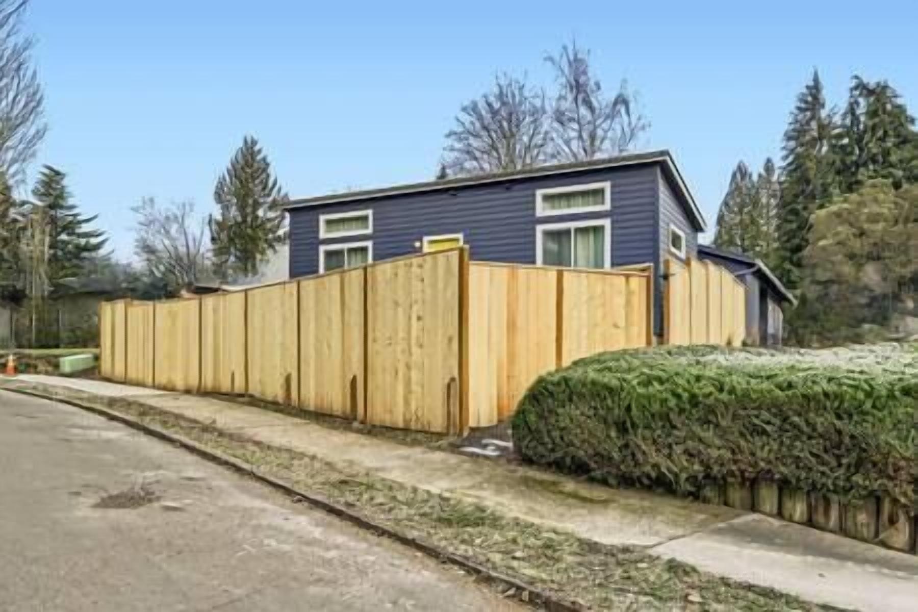 A single-story house with a wooden fence and a well-maintained hedge.
