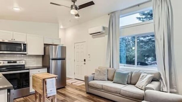 Eine moderne Küche mit Edelstahlgeräten, einem Holzespeisetisch und einer Couch in einem Wohnbereich mit großem Fenster.