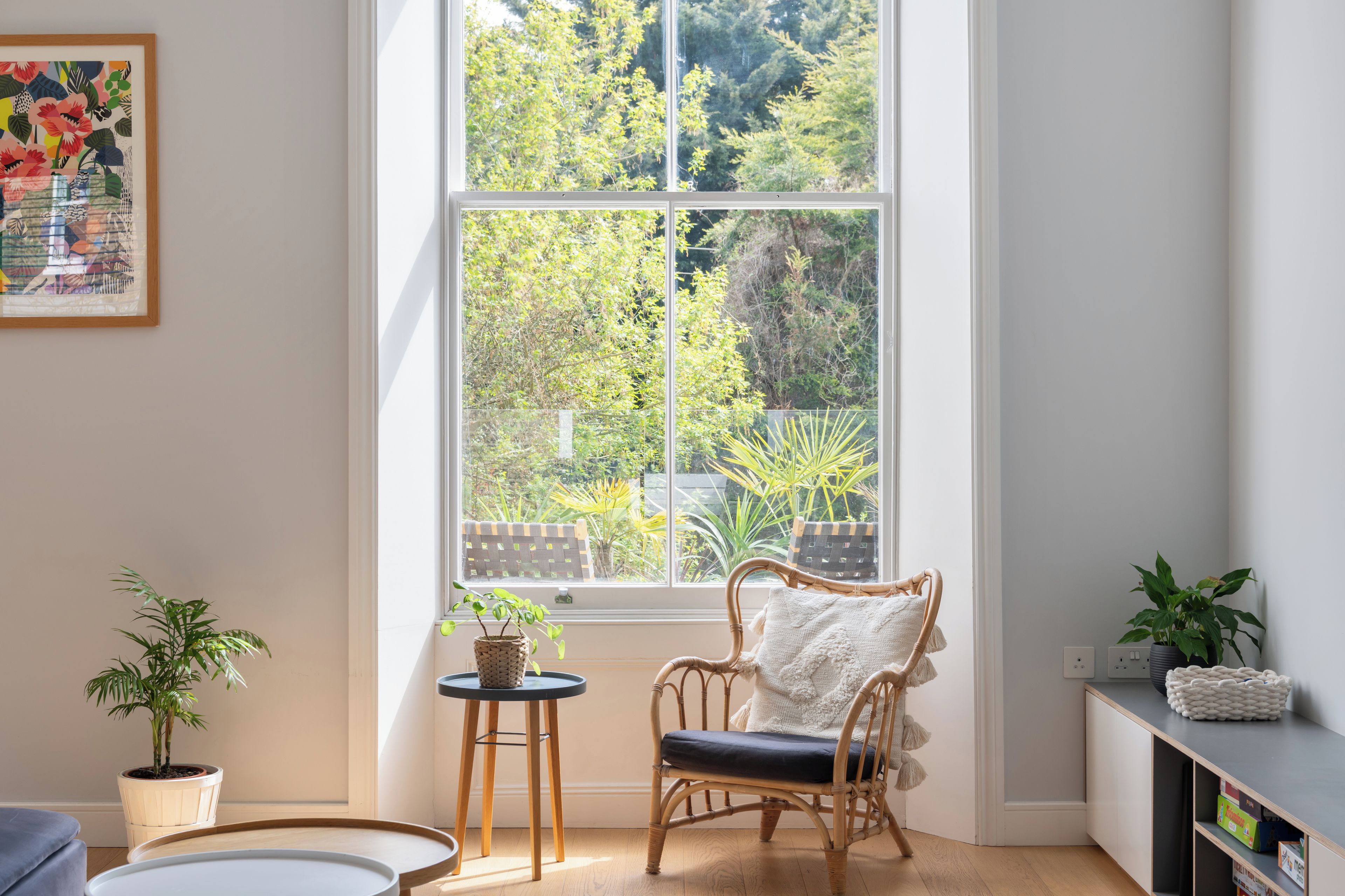 A room with a large window, a wicker chair, a small table, and a potted plant.