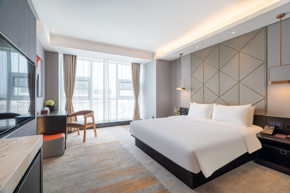 A modern hotel room with a large bed, a desk, a chair, and a TV.