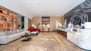 Un moderno hall de hotel con mostrador de recepción, zona de estar y cocina al fondo.