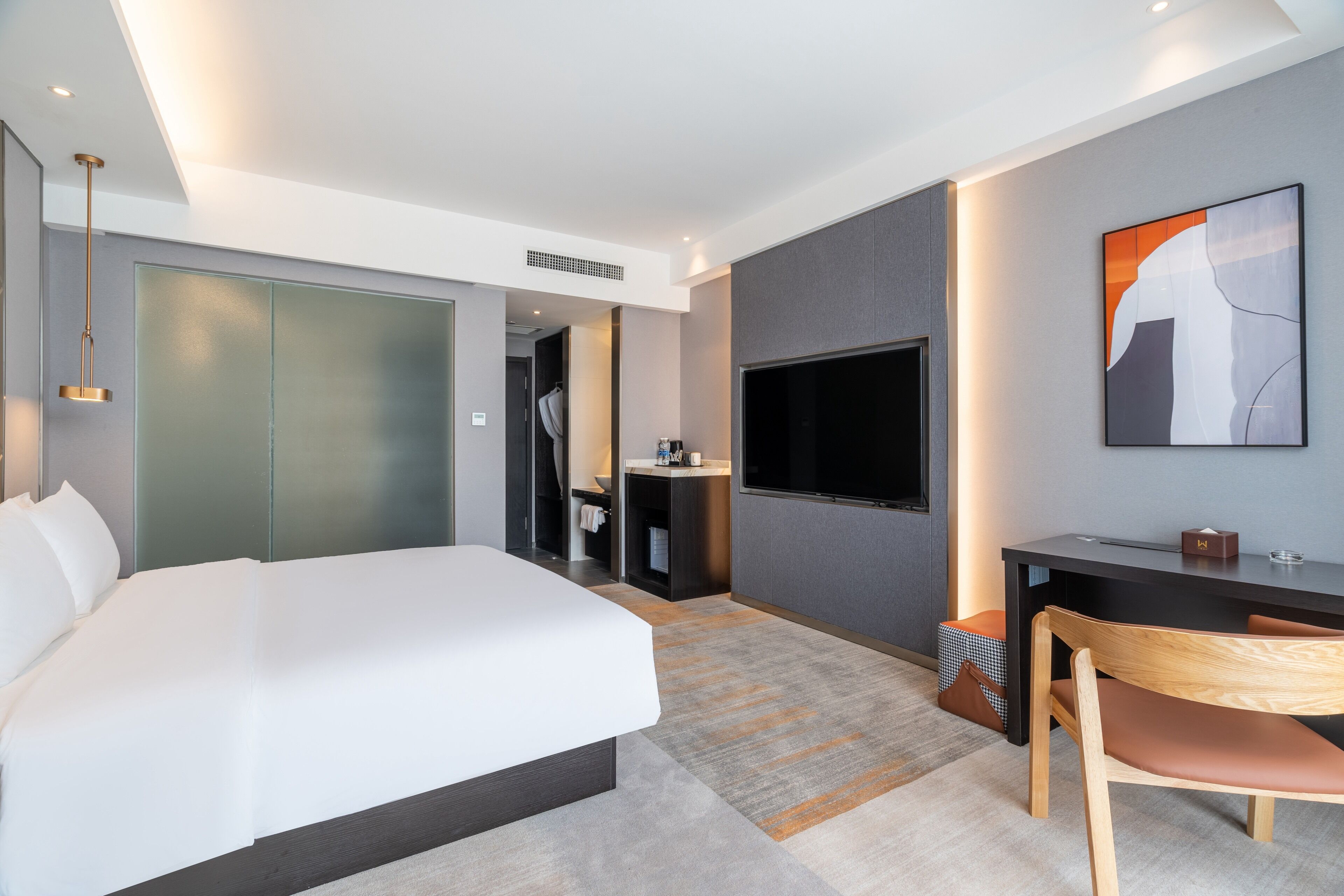 Una habitación de hotel moderna con una cama grande, un escritorio con una silla, un televisor y un cuadro en la pared.