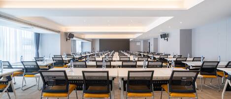 Un salón de conferencias con varias mesas y sillas, equipado con computadoras portátiles y botellas de agua.
