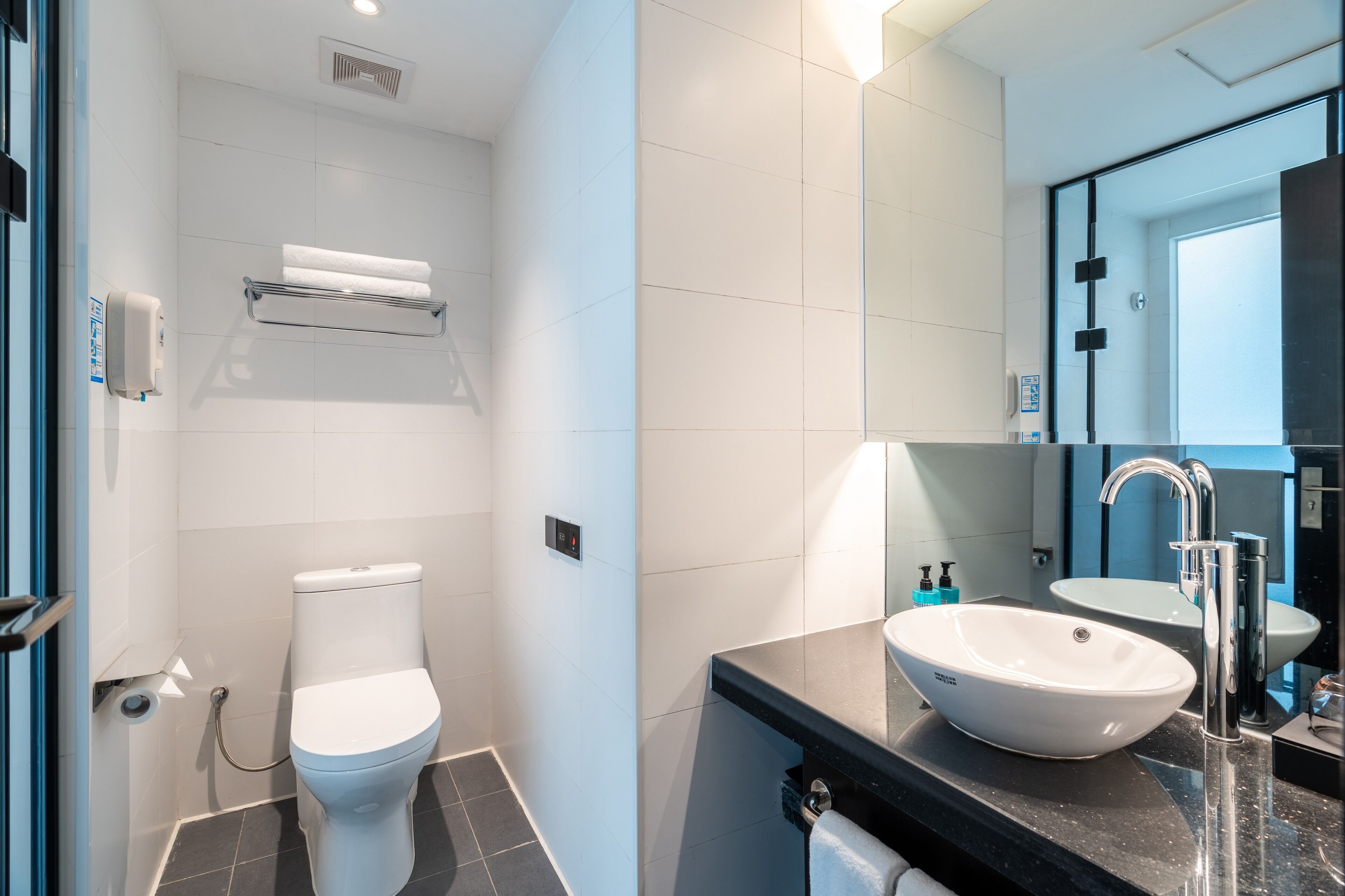 Un baño moderno con un inodoro blanco, un lavabo negro y un espejo.
