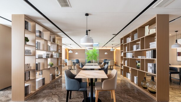 Una biblioteca moderna con suelos de mármol, una mesa central con sillas y estanterías a ambos lados.