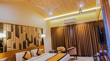 A modern hotel room with a wooden ceiling, a large bed with a geometric headboard, a flat-screen TV, a desk with a chair, and a minibar.