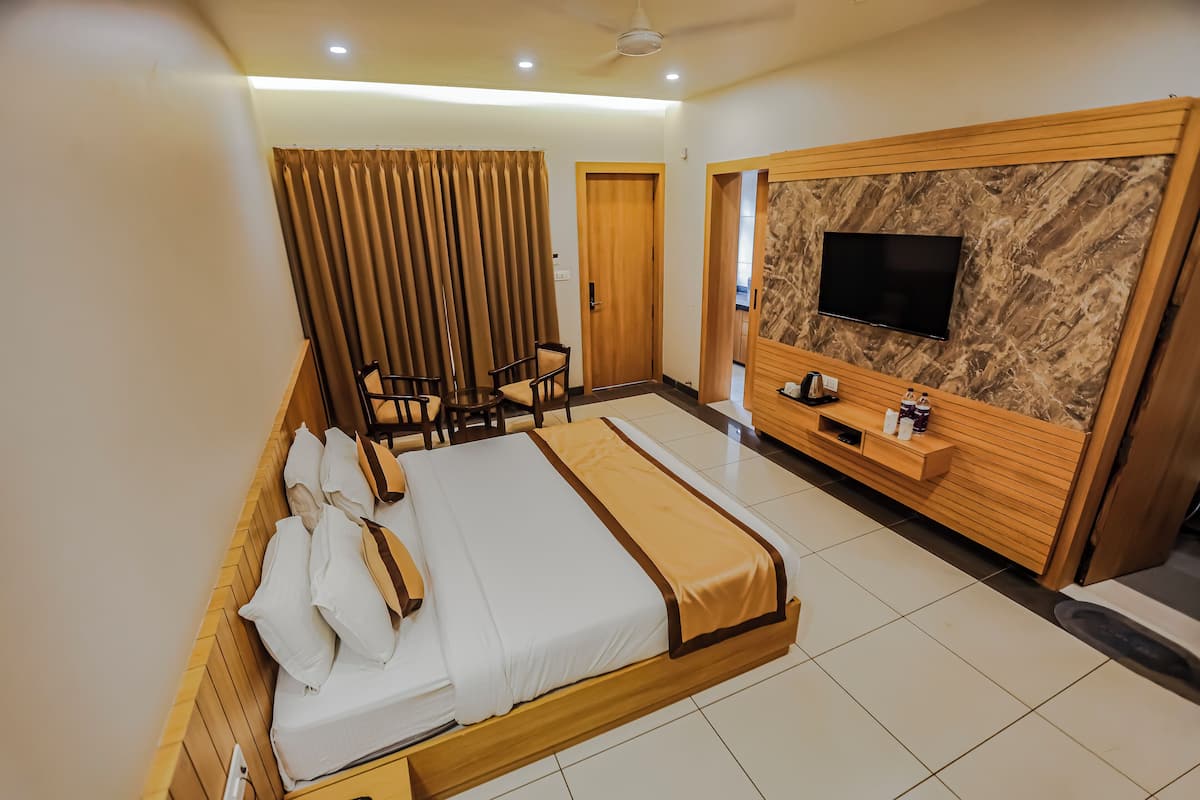 A hotel room with a large bed, a TV mounted on a marble wall, a wooden desk, and a seating area with chairs.
