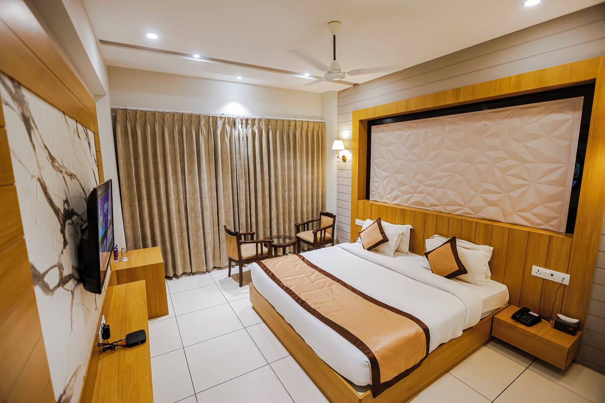 A hotel room with a large bed, a desk with a chair, a TV, and a ceiling fan.