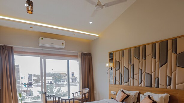 A modern hotel room with a large bed, a balcony with seating, and a city view. - Hotel Mukut Mani Govardhan (Mathura)