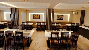 A modern restaurant with high tables and chairs, recessed lighting, and artwork on the walls. - Hotel Mukut Mani Govardhan (Mathura)