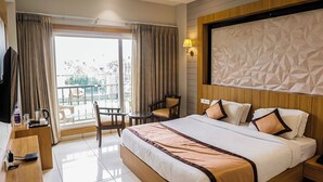 A hotel room with a large bed, a desk, a chair, and a balcony with a view. - Hotel Mukut Mani Govardhan (Mathura)