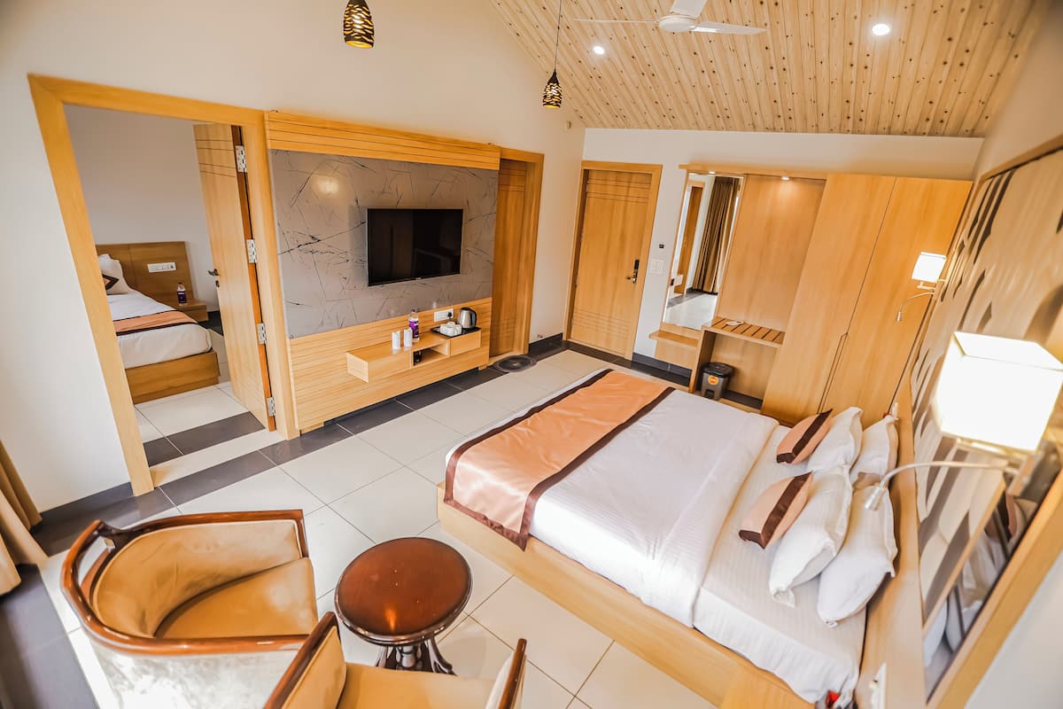 A modern hotel room with a large bed, a TV, a wooden wardrobe, a seating area with a chair and table, and a small bathroom.