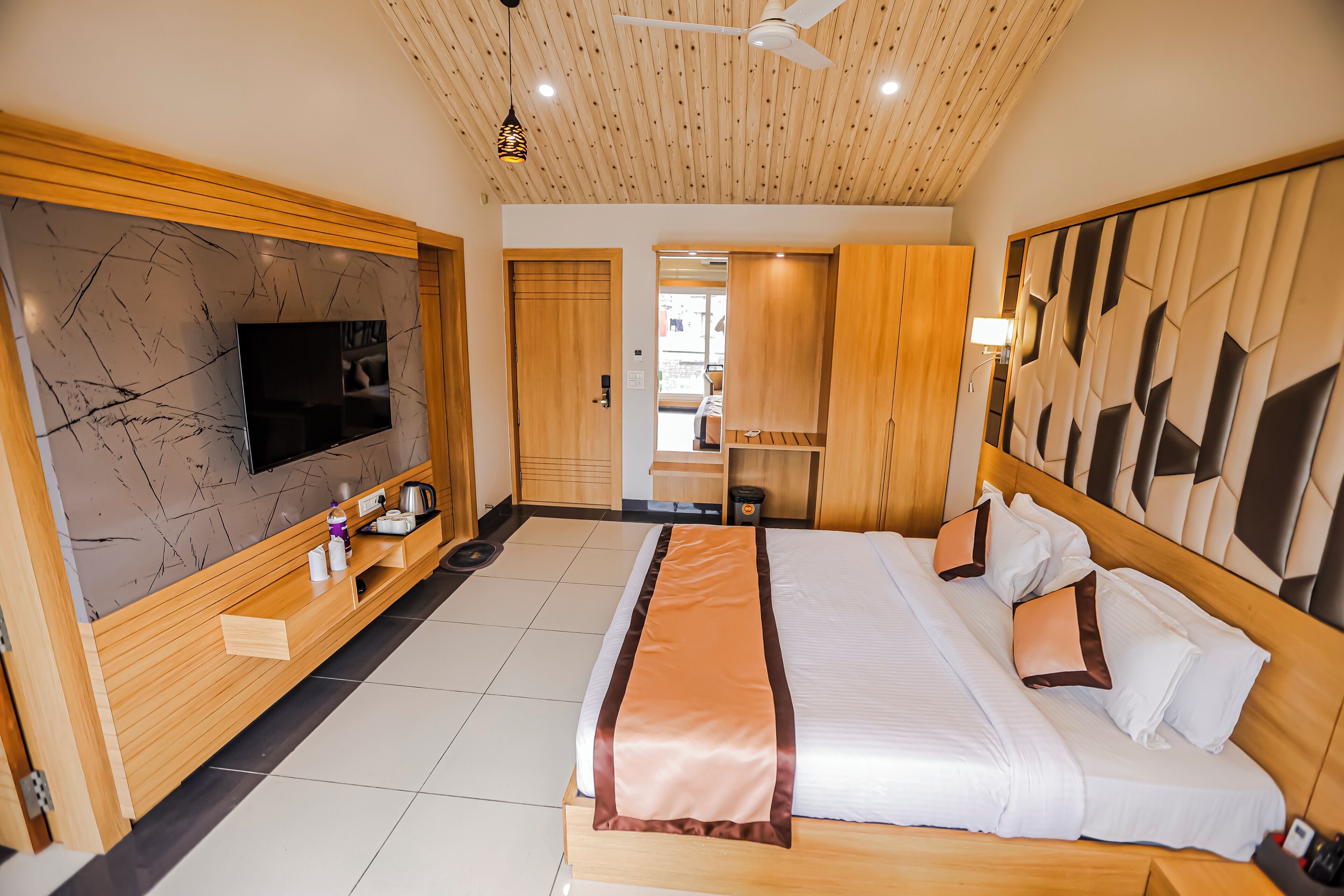 Camera d'albergo moderna con un letto grande, pannelli in legno, televisore a schermo piatto e ventola a soffitto.