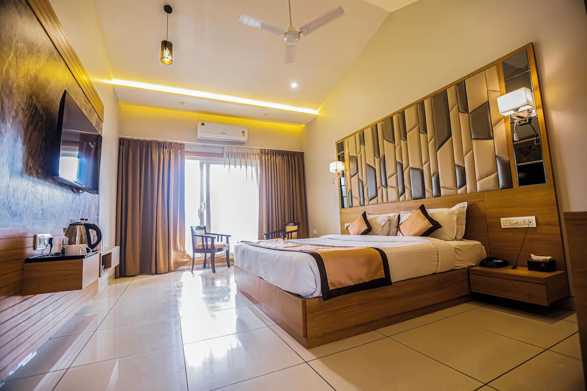 A modern hotel room with a large bed, a flat-screen TV, a ceiling fan, and a view of the outdoors.