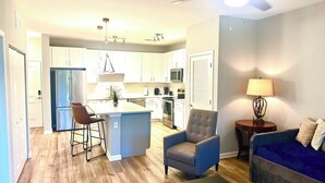 Una sala de estar moderna con un sofá azul, una mesa de centro y un comedor con una cocina al fondo.