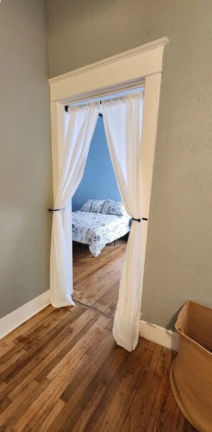 A room with a bed, a wooden floor, and a white curtain. - Historic Downtown Craftsman, 3br/2ba with a yard (Clarksville)