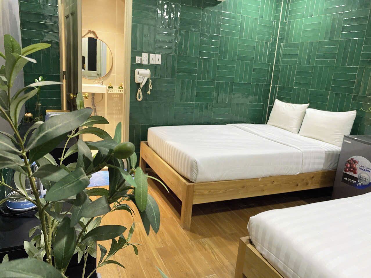 A hotel room with a wooden bed, a bedside table, a mirror, and a green tiled wall.