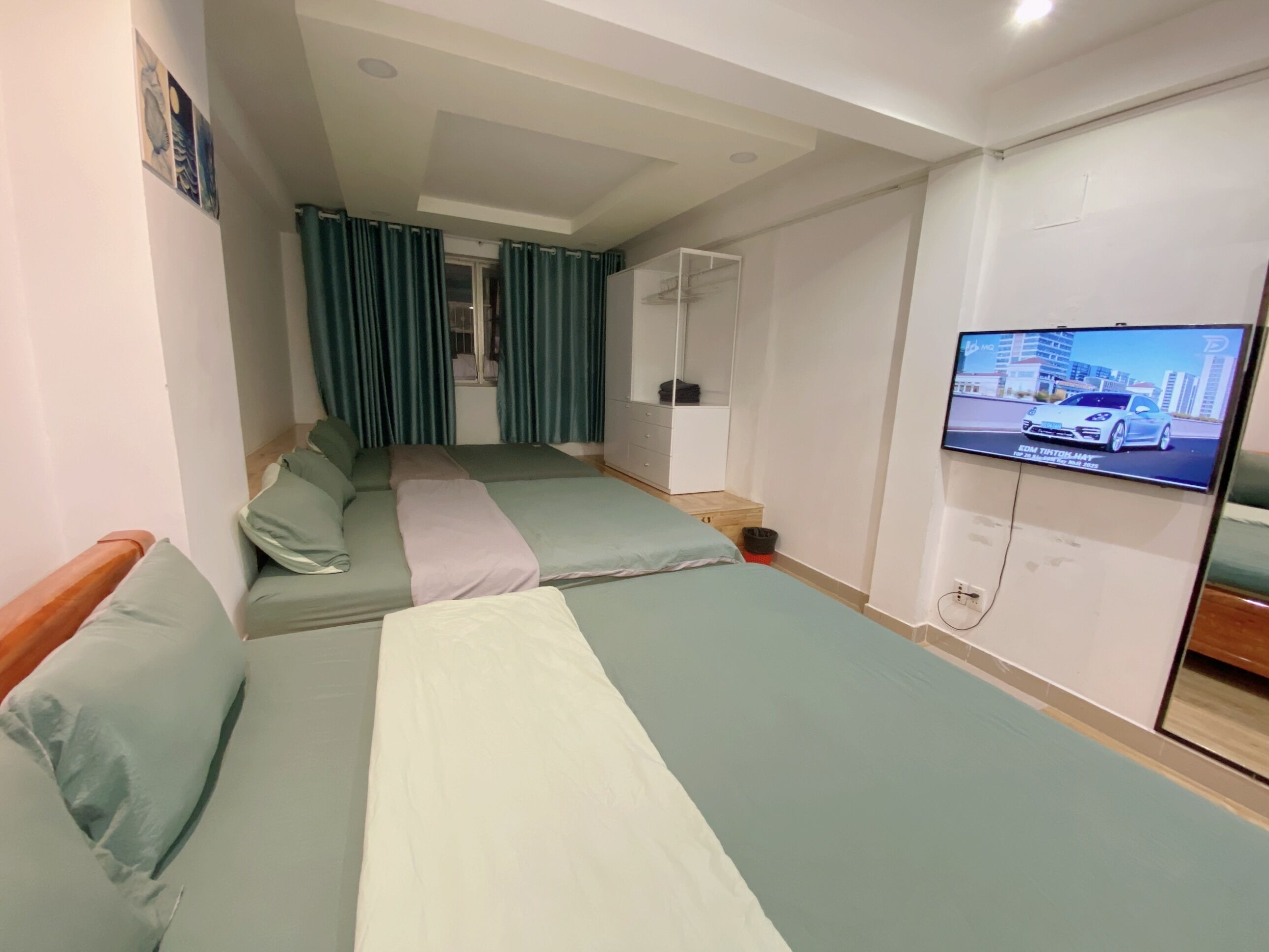 A hotel room with two beds, a television, a wardrobe, and a window with curtains.