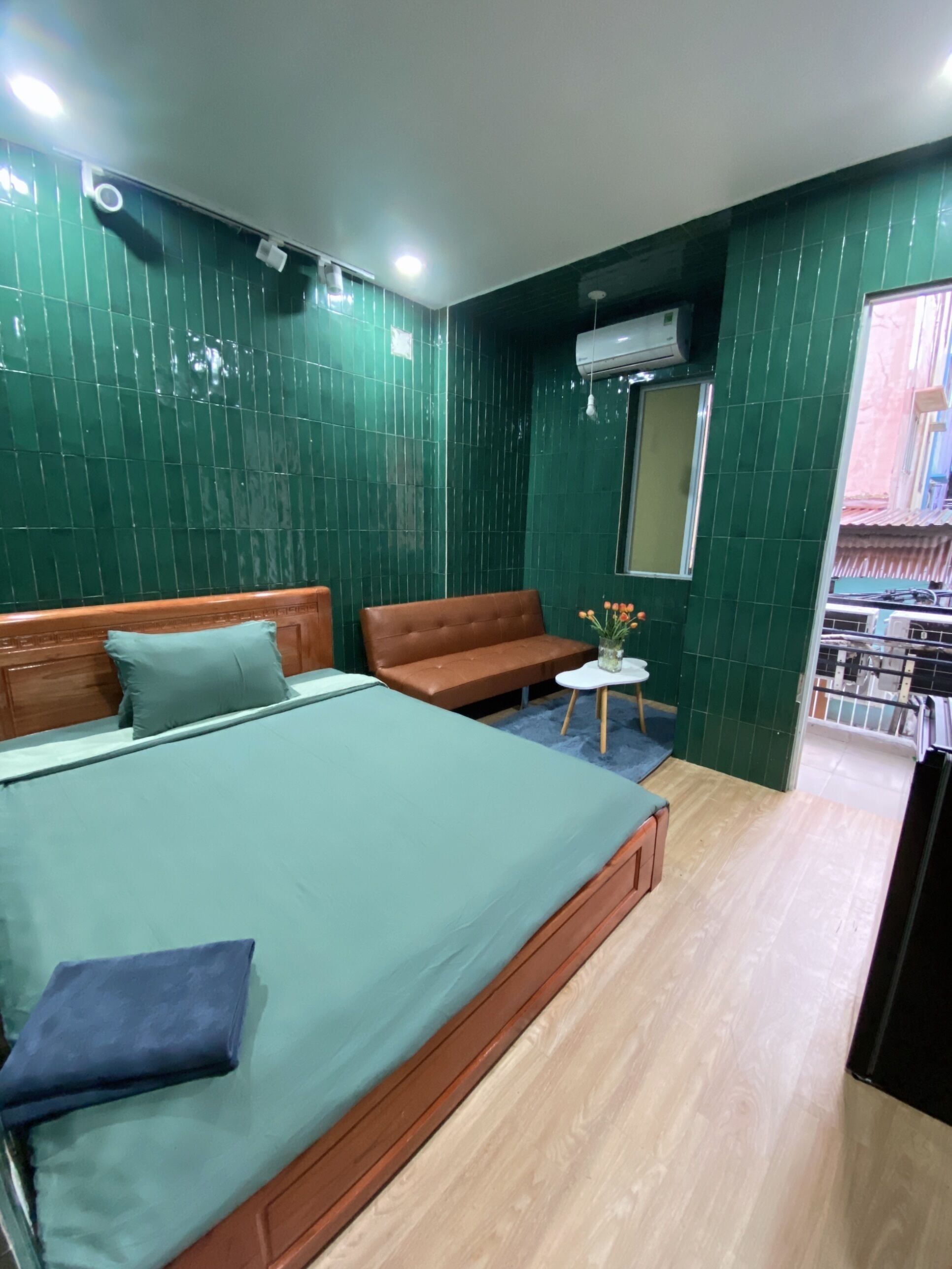 A room with a bed, a sofa, a small table with a vase, and a window.