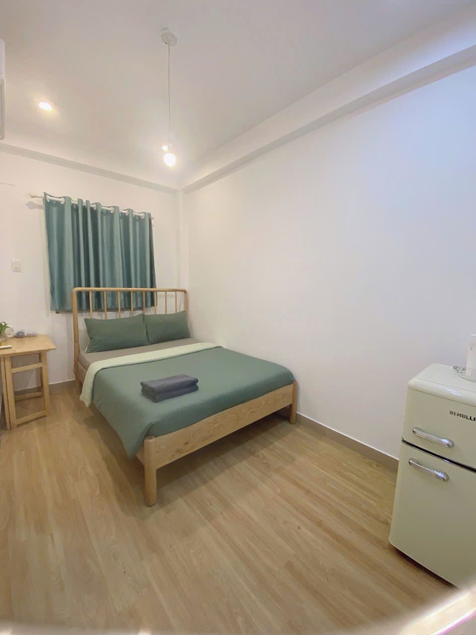A small, neatly arranged bedroom with a wooden bed, a bedside table, a desk, and a white cabinet.