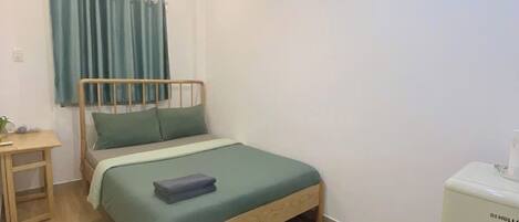 A small, neatly arranged bedroom with a wooden bed, a bedside table, a desk, and a white cabinet.