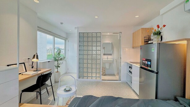 Une chambre compacte et moderne, équipée d’un lit, d’un bureau, d’une chaise, d’une petite table, d’un réfrigérateur et d’une fenêtre.