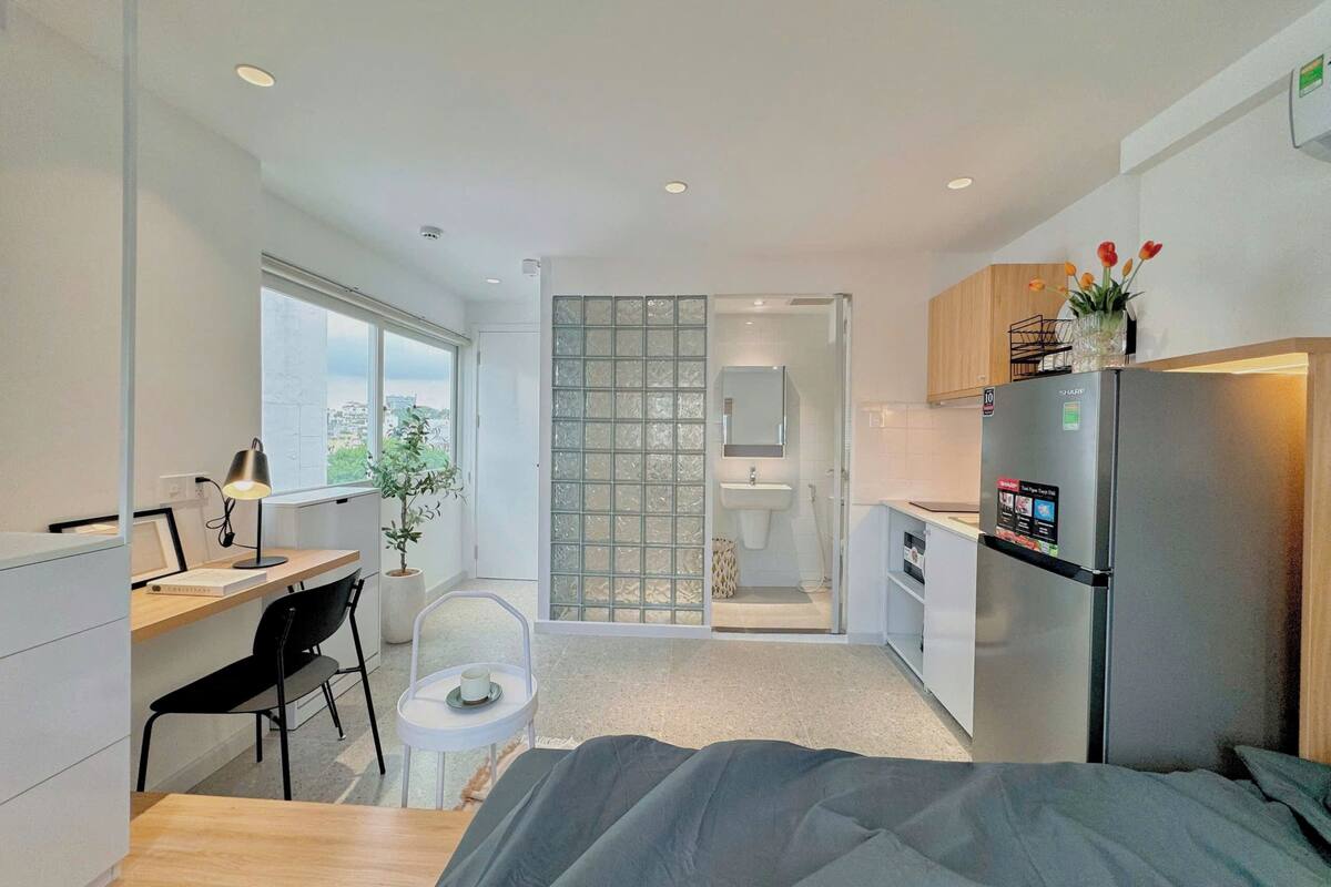 Une chambre compacte et moderne, équipée d’un lit, d’un bureau, d’une chaise, d’une petite table, d’un réfrigérateur et d’une fenêtre.