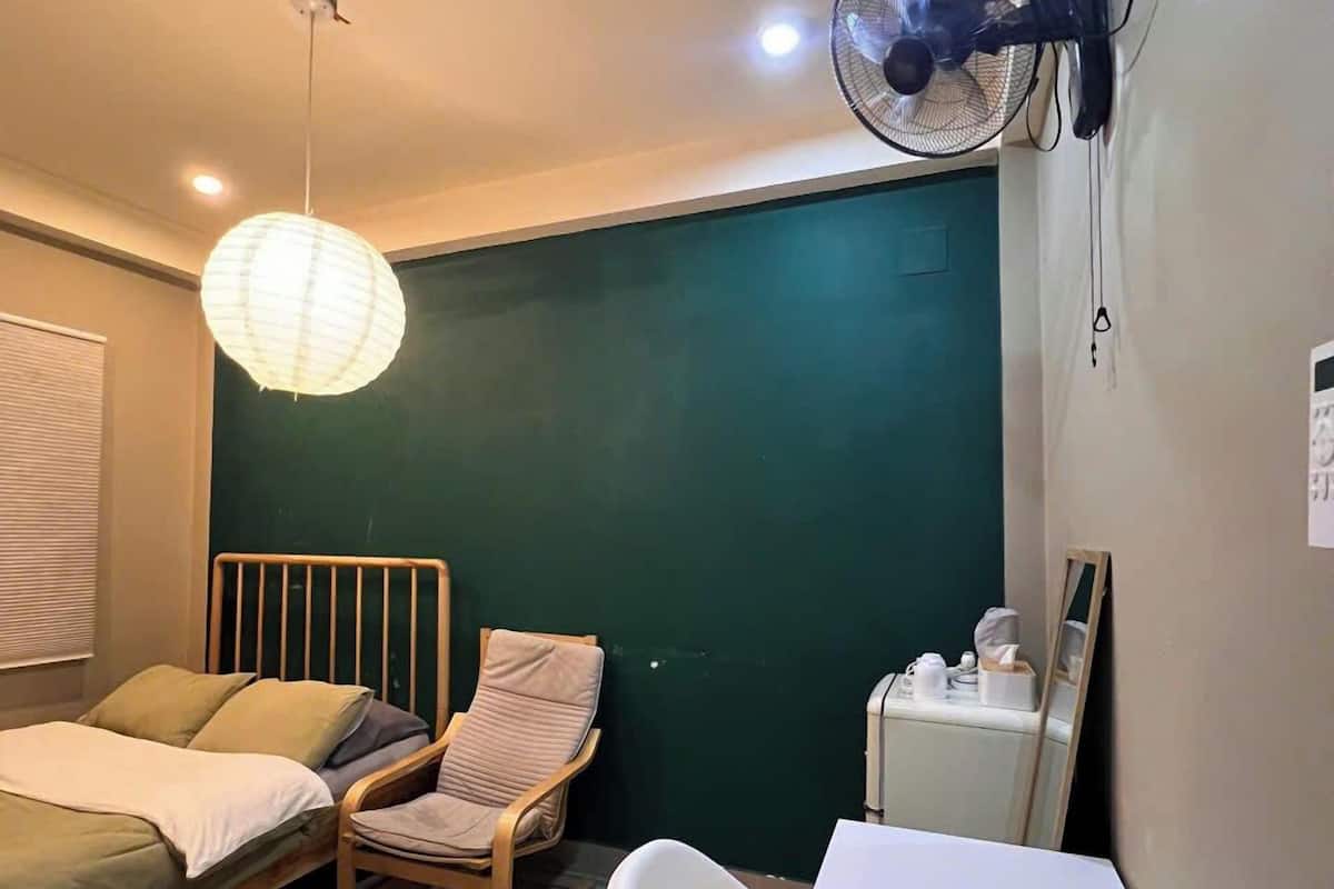 Une pièce comprenant un lit, une chaise, un bureau, un ventilateur et un luminaire suspendu.