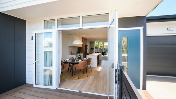 Una casa moderna con comedor, cocina y un amplio ventanal corredizo que da a un espacio exterior.