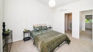 Un dormitorio con cama, mesitas de noche, una lámpara y una puerta que da a un baño.