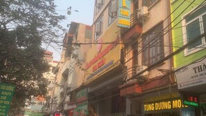 A street view with multiple buildings, some with signage indicating businesses. There are motorcycles parked along the street, and a few pedestrians. - Tung Duong Motel HN -BAYLUXURY (Hanoi)